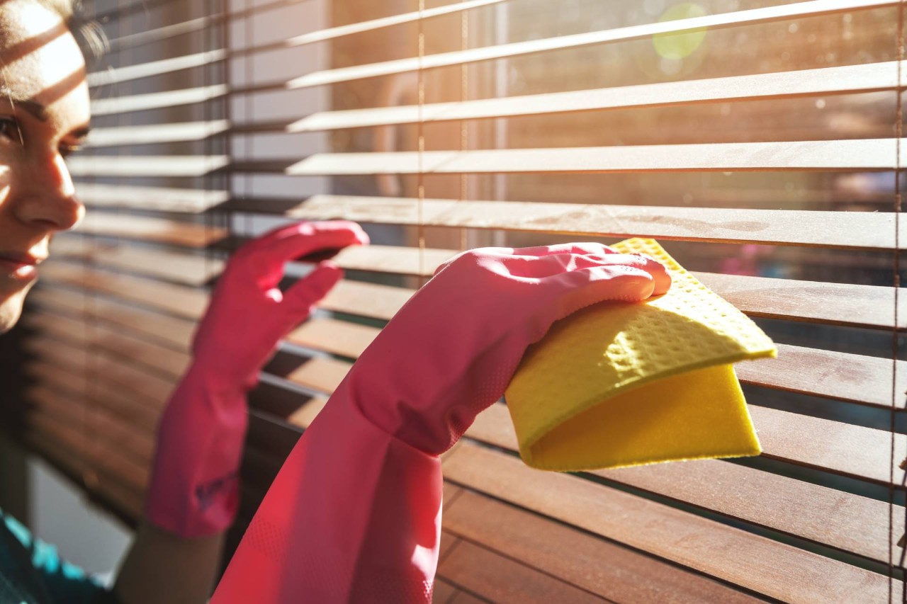 Person cleaning their wooden blinds with a yellow cloth near Kailua Kona, HI